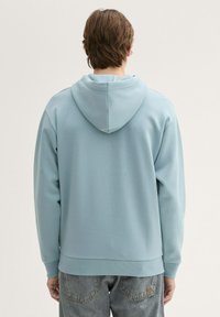 Felpa con cappuccio azzurro chiaro in tessuto morbido e liscio, con tasca a marsupio, polsini e cinturino a coste. Vestibilità informale e rilassata.