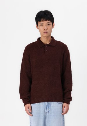 Pull en maille texturée marron avec col, trois boutons et manches longues légèrement sur taillées, associé à un jean en denim bleu clair.