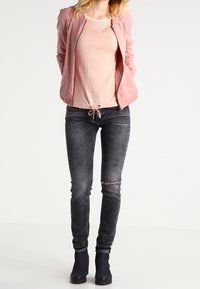 Jasnoróżowa bomberka, beżowa koszula z sznurkiem, ciemnoszare dopasowane dżinsy z przetarciami oraz czarne botki za kostkę.