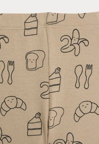 Pantaloni da pigiama beige con disegni a tema alimentare neri, tra cui pane, cornetti e torta, dotati di una texture a coste e una cintura elasticizzata.