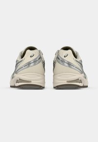 Lysebeige løpesko med et teksturert mesh-overdel, sølvfargede detaljer og en polstret såle. Har en bakre trekkflik og logodetalj.