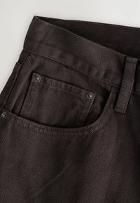 Close-up of dark brown denim jeans showing front pocket, small coin pocket with rivets, belt loop, and waistband stitching details.