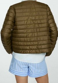 Giacca imbottita marrone con un design trapuntato, caratterizzata da un collo tondo e una lunghezza leggermente corta, abbinata a pantaloni corti a righe blu chiaro.