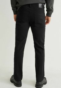 Jean noir à coupe droite, fabriqué à partir d'un mélange de coton extensible, avec poches standard et un détail en cuir à l'arrière.