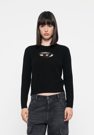 Maglione nero a maglia con un design aderente, caratterizzato da un distintivo taglio ovale sul petto e maniche lunghe. Abbinato a pantaloni cargo scuri.