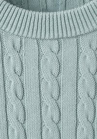 Light blue knitted fabric with prominent cable knit patterns and a thick ribbed collar at the top.