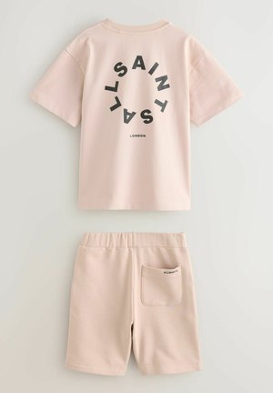 Šviesiai rožinė medvilnės dviejų dalių komplektas, kuriame yra trumpomis rankovėmis marškinėliai su juodu apvaliu tekstu ir suderinti šortai su užpakaline kišenėle.