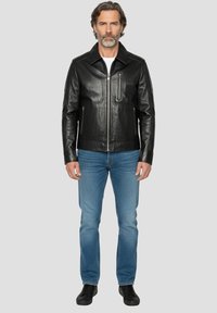 Zwarte leren jas met een gestructureerde kraag, een rits aan de voorkant en een zak met rits; gecombineerd met een blauwe spijkerbroek en zwarte schoenen.