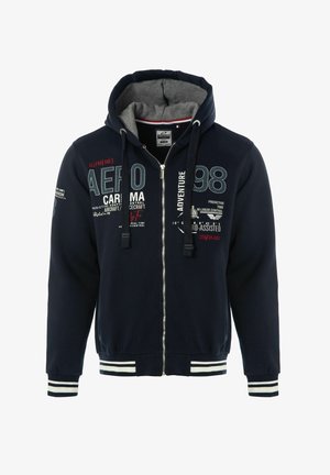 Sweat à capuche zippé bleu marine avec intérieur gris, présentant des accents à rayures blanches aux poignets et à l'ourlet. Texte décoratif et graphismes en plusieurs couleurs.