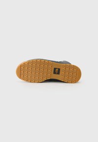 Black footwear outsole with a textured, rubber surface. Features a raised pattern and an orange tread for grip. Prominent logo in center.