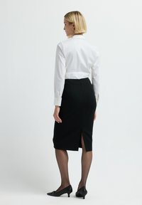 Weißes Langarmhemd, schwarze Bleistifthose mit einem Schlitz hinten und schwarze Kitten-Heels. Geschmeidige Stofftextur, klassischer Schnitt und Design.