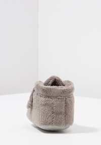 Grijze fuzzy pantoffel met een zachte textuur, ronde vorm en een opgerolde boord. De zool is vlak met subtiele stikseldetails.