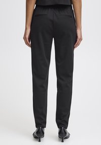 Black, tailored pants with a smooth, matte finish, featuring back pockets and a fitted design, complemented by black, heeled shoes.