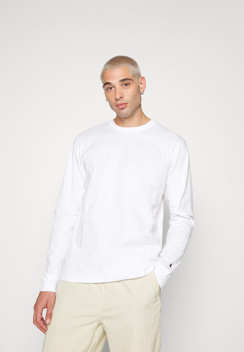 Wit katoen shirt met lange mouwen en een ronde halslijn, voorzien van een klein logo op de linker mouw, gecombineerd met beige broek.