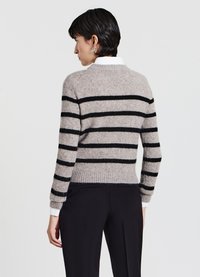 Maglione a righe grigie e nere in morbido materiale, con scollo tondo, polsini a costine e silhouette aderente. Indossato con pantaloni scuri.