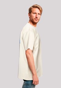 Crème-kleurig oversized t-shirt met korte mouwen, voorzien van een grafisch ontwerp op de achterkant en een relaxte pasvorm. Katoenen stof, eenvoudige textuur.