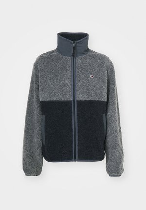 Giacca in fleece grigia e nera con colletto alto, zip frontale e tessuto testurizzato. Dotata di un patch con logo e tasche laterali.