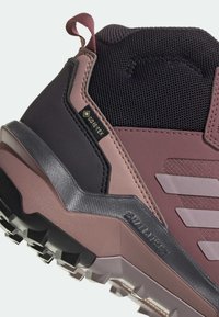 Gros plan d'une chaussure de randonnée marron et noire avec une semelle texturée, une étiquette Gore-Tex, une languette et un col de cheville rembourré pour une utilisation en extérieur.