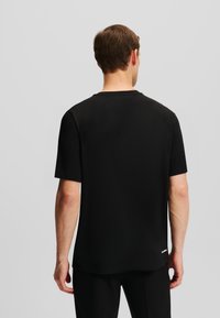 Tricou scurt cu maneci negre, din bumbac, cu guler tip crew și un detaliu discret al logo-ului la tivul inferior. Textură mătăsoasă, croială lejeră.