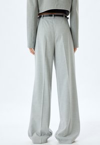 Lichtgrijze high-waisted broeken met een losse pasvorm, geplooide voorkant en subtiele textuur. Gecombineerd met een cropped jack en een zwarte riem.