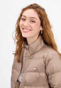 Jasnobrązowa kurtka puchowa z wysokim kołnierzem i gładką fakturą. Posiada małe logo Levi's i zamek błyskawiczny.