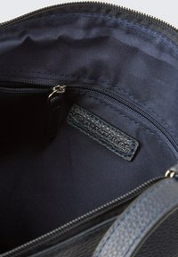 Schwarzes, strukturiertes Lederinnere der Tasche mit einem glatten, marineblauen Stofffutter, das eine Reißverschlusstasche und ein Markenlabel in der Ecke aufweist.