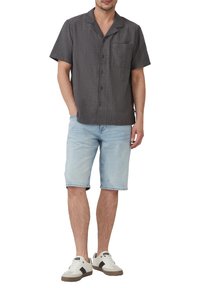Kurzarm, kragenloses Hemd in Dunkelgrau mit einem dezenten Muster, kombiniert mit hellblauen Jeansshorts und weißen Sneakers mit dunklen Akzenten.