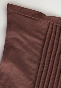 Bruin textiel met een zichtbare structuur en plooien langs één rand, met een subtiele glans en netjes gestikte randen.