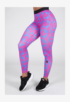Leggings à motifs rose et bleu avec une taille haute, fabriqués dans un matériau extensible, associés à des chaussures de sport noires.