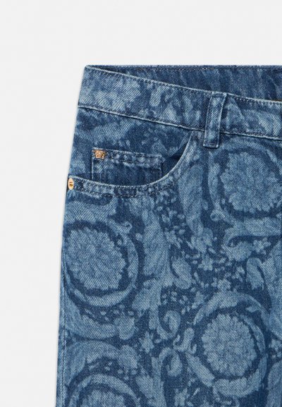 Τζιν παντελόνι με σχέδιο πλύσης οξέος σε σκούρο μπλε χρώμα, μικρή μπροστινή τσέπη, θηλιά για ζώνη και χρυσή λεπτομέρεια ριβέτα στην αριστερή πλευρά της λεκάνης.