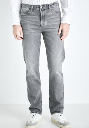 Grå denimjeans med rett snitt, med fem lommer, knapperegn og subtile slitasje. Kombinert med hvite joggesko.
