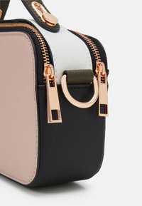 Mała prostokątna torebka o czarnej, teksturowanej podstawie, różowym bocznym panelu, białym wierzchu oraz zamkach i akcentach w kolorze różowego złota.