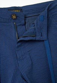 Pantalones a rayas azules con cierre de cremallera y botón, que presentan una textura de tela suave y un forro interior azul en contraste.