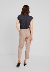 Mörkblå blus med polka-dots och ärmar som är avskurna, ihop med beige avsmalnande byxor. Byxorna har elastisk midja och uppvikta fållar. Svarta klacksandaler.