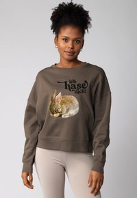 Vrouw in een bruine sweatshirt met een opgerold konijn en de Duitse tekst "ich hase dich!" gedrukt op de voorkant.