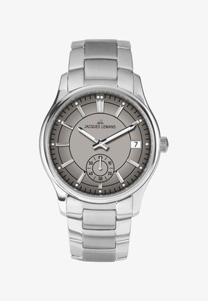 Sudraba krāsas nerūsējoša tērauda pulkstenis ar apaļu pelēku ciparnīcu, stundas atzīmēm, apakšciparnīcu un datuma rādītāju pie pulksteņa trīs stundu pozīcijas; metāla aproce.