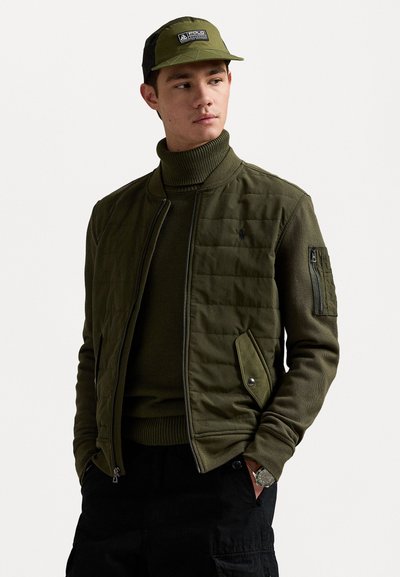 Maslinasto zeleni bomber jakna s kvadratnim teksturom, zatvaranjem na patentni zatvarač, rebrastim ovratnikom i bočnim džepovima. Nosena s odgovarajućim turtleneckom i kapom.