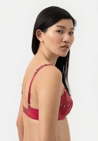 Rode bh met bloemachtige borduursels, verstelbare bandjes en een haak-en-oogsluiting. Het materiaal lijkt glad met een delicate textuur.