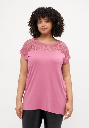 Tricou roz cu un design texturat din dantelă la yoke, mâneci scurte și o croială lejeră. Material neted cu o linie curbată la baza tricoului, combinat cu leggings negri.