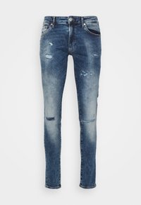 Jeans de denim de corte ajustado en azul medio con detalles desgastados, un sutil desvanecido, cinco bolsillos y herrajes metálicos en la cintura.