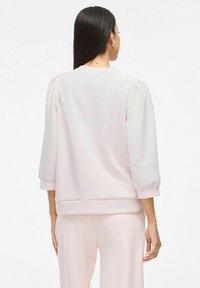 Felpa rosa chiaro con maniche a sbuffo a tre quarti e orlo a coste. Tessuto liscio, design minimalista e senza motivi visibili.
