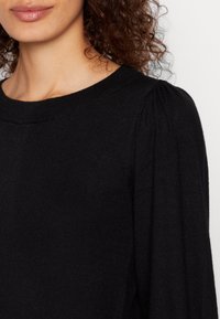 Maglione nero in maglia con scollo rotondo, caratterizzato da maniche leggermente gonfie e da una texture morbida, che presenta un design minimalista.