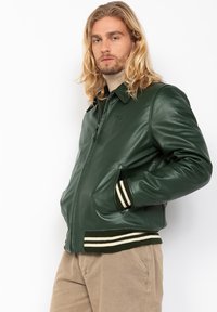Groene leren bomberjack met een kraag, zijzakken en gestreepte ribgebreide cuffs en zoom. Glad textuur en aansluitend ontwerp.