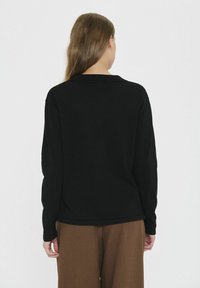 Svart långärmad topp med krage, gjord av mjukt tyg, visad bakifrån, ihopparad med bruna vida byxor.