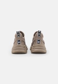 Hnědé síťované tenisky s texturovaným povrchem, vybavené zádovým páskem a kontrastním černým poutkem s bílým nápisem. Zaoblená podešev.