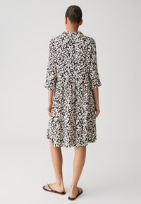 Black and white patterned dress with a tiered skirt, three-quarter sleeves, and a collar. Made from lightweight fabric, casual design.