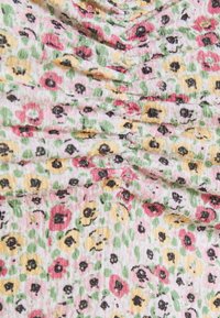 Tissu floral avec de petites fleurs roses, jaunes et noires sur un fond texturé rose clair, avec des détails froncés.