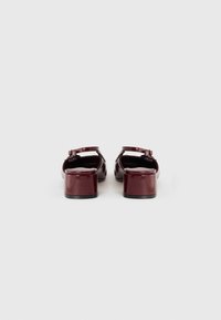 Sandales en cuir verni bourgogne avec un talon épais, une sangle de cheville ajustable et un design ouvert à l'arrière. Fini lisse avec une texture brillante.