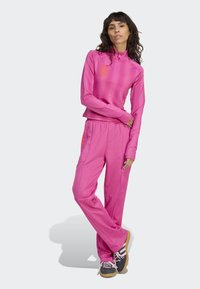 Roze sportieve trainingspak met een ritskraag, slim-fit lange mouwen en bijpassende broek met zijzakken en contrasterende oranje accenten.