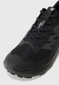 Black athletic shoe featuring a textured upper, synthetic materials, pronounced toe cap, and a contrasting logo with laces for secure fit.